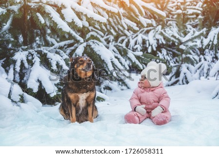 Portrait of a little baby girl with a dog on the snow in the forest in winter. Baby and dog are best friends. 