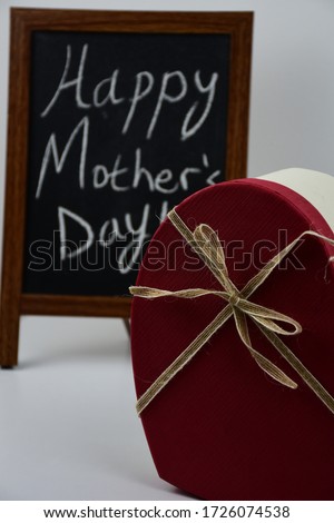 Happy mother's day written on 
black board next to flowers and present box.