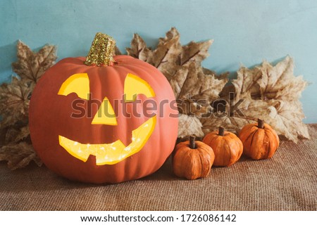 Happy Halloween Pumpkin with a smile and decorations on a rustic burlap table with blue background with copy space.  A horizontal with a side view.