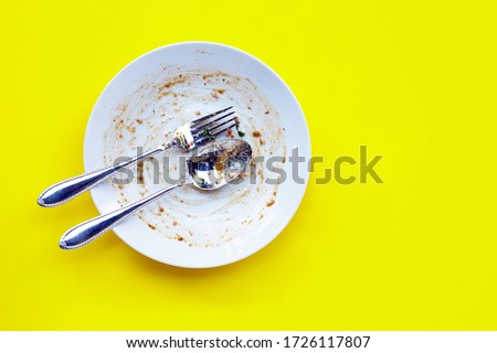Dirty dish with spoon and fork on yellow background. Copy space