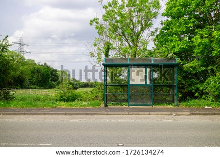 Bus stop on the side of a lane/road, in the countryside, or rural area. Bus stop is empty. It's a sunny Summer day, with a blue sky in the background. There's green grass and trees. Royalty-Free Stock Photo #1726134274