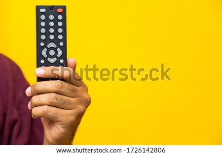 Close up male hand holding television remote control on isolated yellow background.