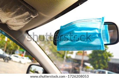 Blue surgical mask hanging on rear view mirror with blurred background.