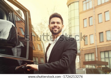 Handsome young man opening door of modern car outdoors
