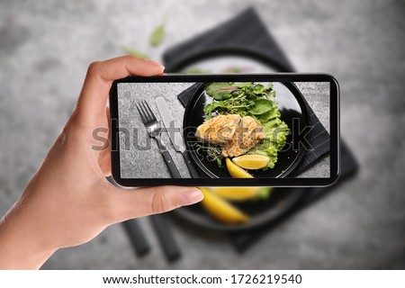 Blogger taking picture of delicious grilled fish at table, closeup. Food photography