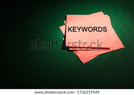 Pink paper card with phrase KEYWORDS on dark green background, above view. Space for text
