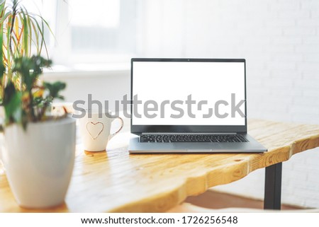 Opened laptop notebook with white screen on wooden table against window at home, mock up