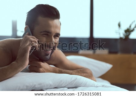 Cheerful handsome guy is still lying in bed and talking on cell phone stock photo. Website banner