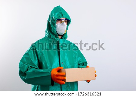Man in a hazmat suit wearing rubber gloves and holding a cardboard box. Website banner stock photo