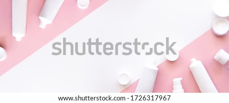 White squeeze tubes, bottles of moisturizing cream flat lay on pink and white background top view copy space. Mock-up templates. Beauty skincare, natural cosmetic, daily products. Banner stock photo.