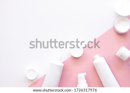 White squeeze tubes, bottles of moisturizing cream flat lay on pink and white background top view with copy space. Mock-up templates. Beauty skincare, natural cosmetic, daily products. Stock photo.