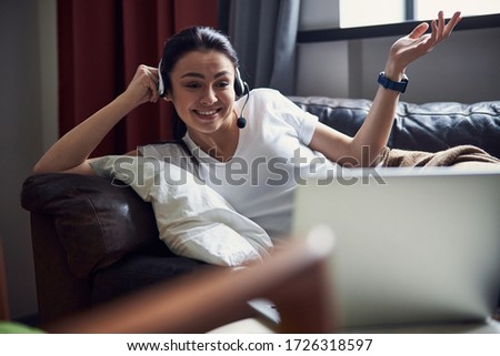 Caucasian smiling woman laying on coach opposite laptop at home stock photo. Modern technology concept