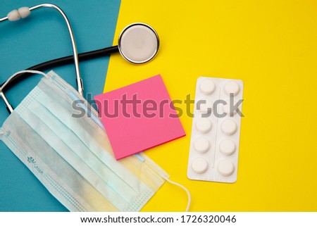Stethoscope, tablets and pink sticky note for text above face mask on colorful background