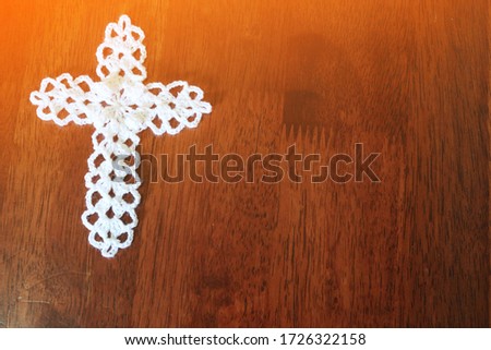  Top view of white crochet cross on grunge wooden table background in orange sunlight & sun rays from window. Xmas, Jesus is Risen & Easter day concept, copy free space                              