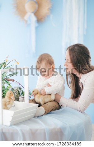 Stock Photo -  Mom and baby play indoors in spring. Decorated home and spring flowers. Family celebrating Easter