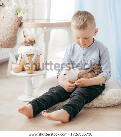 Stock Photo -  Little boy play with gosling and rabbit indoors in spring. Decorated home and spring flowers. Family celebrating Easter