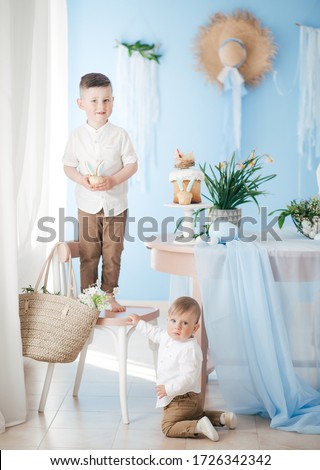 Stock Photo -  Boys play with rabbit indoors in spring. Decorated home and spring flowers. Family celebrating Easter