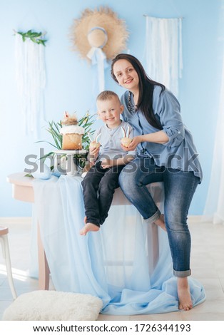 Stock Photo -  Little boy and mom play with gosling and rabbit indoors in spring. Decorated home and spring flowers. Family celebrating Easter