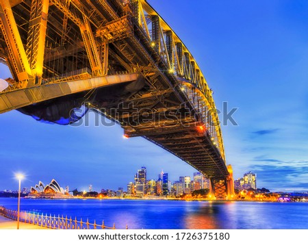 Underbelly of steel arch of the Sydney harbour bridge across harbour at sunset to city CBD.