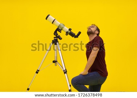 Amateur astronomer looking at the stars with a telescope. Astronomy and astrology concept. Studio shot on a yellow background.