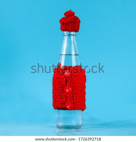 A glass bottle with cold water is dressed in a hat and a warm jacket. The concept of heat and frost.