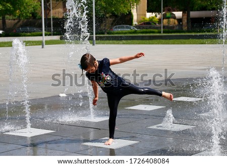 girl runs and plays in the spray of a city fountain