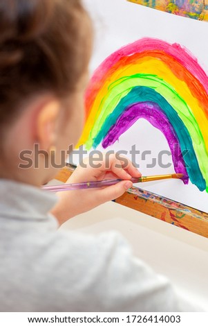 Child is drawing rainbow with watercolors on the sheet of paper on the easel. Creativity concept.