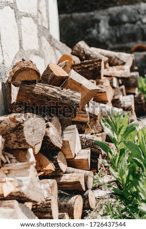 Wood folded in a row near a stone wall and grass