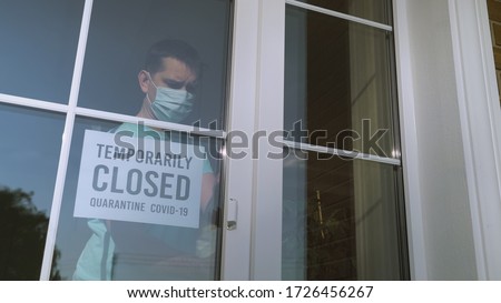 Small business owner turns the sign on her storefront from open to closed because of coronavirus pandemic. Sign in a shop window: TEMPORARILY CLOSED. Covid-19 isolation and closed shops.
