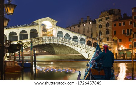 Gondolier carries tourists on gondola Green Canal at dusk - Gondola near Rialto Bridge - Venice, Italy