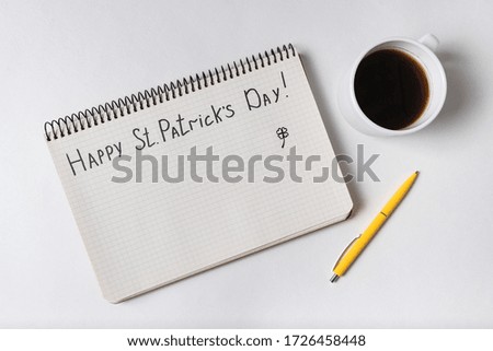 Notebook with words HAPPY St PATRICKS DAY. Coffee and pen. Top view, white background.