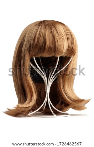 Subject shot of a natural looking blonde wig with bangs and twisted strands fixed on the white metal wig holder. The stand with the wig is isolated on a white background.   Royalty-Free Stock Photo #1726462567