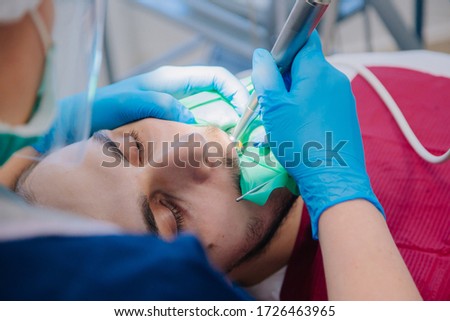 A dentist in blue gloves drills the teeth of a young guy in a dental office. Workflow at the dental clinic