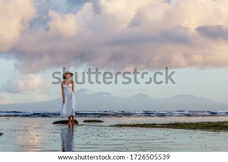 Beautiful young woman by the ocean at sunset time