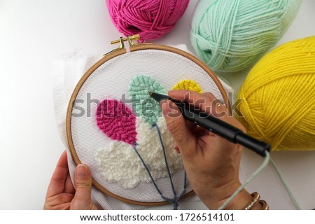 hands of an embroiderer  embroidering balloons in the clouds with the punch needle technique Royalty-Free Stock Photo #1726514101