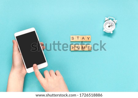 Flatlay concept stay at home, remote order via the mobile app, white alarm and letters wooden cube on blue background. Selective focus.