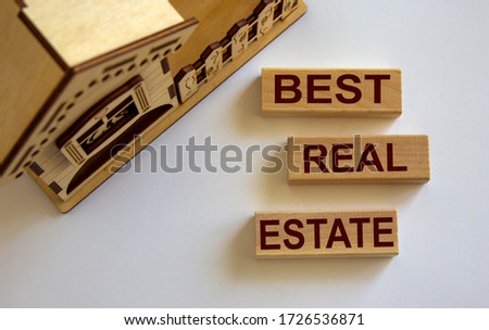 Wooden blocks form the words 'best real estate' near miniature house. White background.