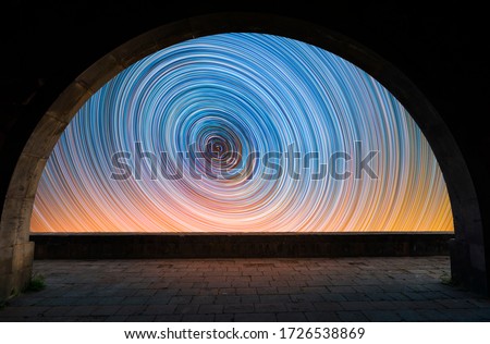 Beautiful night landscape. View from the arch to the colorful star trails on the sky. Night time lapse photography.