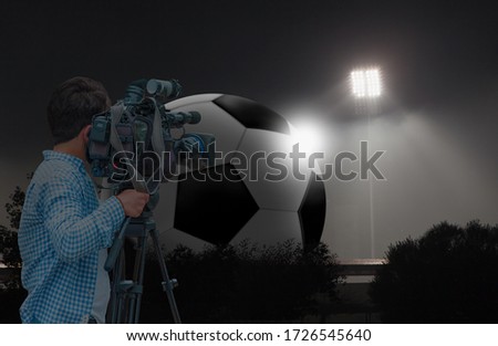 Cameraman shooting live broadcast from to television and internet, giant projector and giant soccer ball in the background
