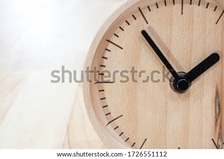 The close-up picture of the wooden table clock with a black dial showing about 2 o'clock on the wooden table as a background with warm light