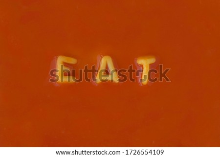 Orange pasta letters spelling the word "Eat" in red tomato sauce viewed from above