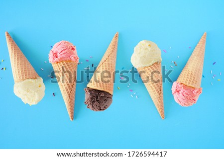 Ice cream cone flat lay over a blue background. White vanilla, pink strawberry and dark chocolate flavors.