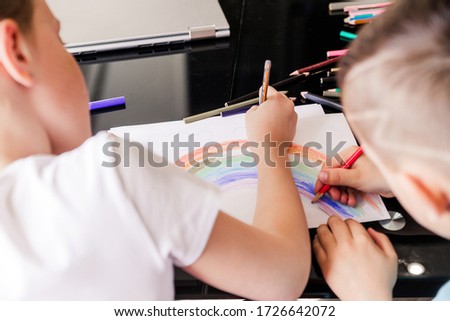 Boy and girl, brother and sister draw a rainbow together with pencils on a white sheet of paper