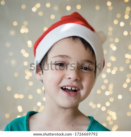 Portrait of child in santa hat. New Year, Christmas, winter, dentistry concept. Lights in the background. Emotional kid face. Cute, funny person. Festive mood. Smiles. Eye contact. Selective focus.
