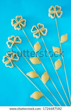 Pattern of raw pasta in the form of flowers: heart shaped pasta, conchiglie, spaggetti on the bright blue paper background. Flat lay. Concept photo