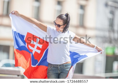 Female fan of Slovakia laughs at wind playing with the flag she holds behind her back.