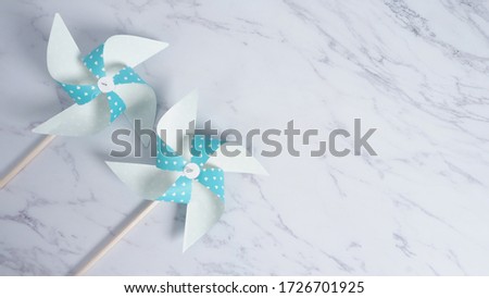 Wind wheel paper real toy on white color marble stone background which made from origami hand made on light blue colour japanese special material and wood stick for baby or kids playing.
