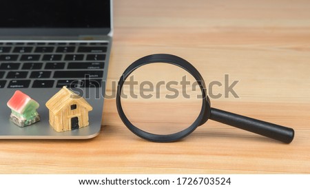Hand holding a magnifying glass over a home model.
Finding a house. Search for housing. 