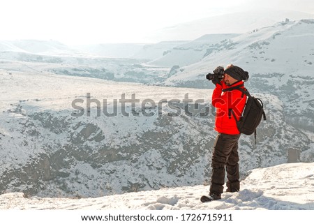 man in red coat takes photos on snowy terrain