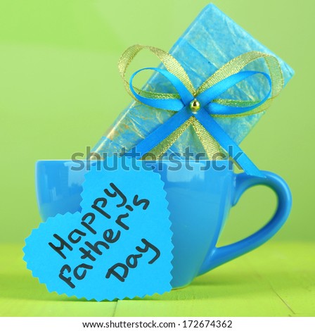 Happy Fathers Day tag with gift box and cup, on wooden table, on light background
